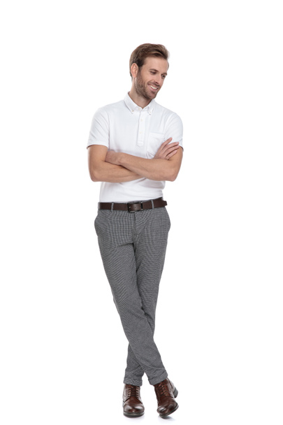 young casual man standing with hands crossed and looks down, smiling on white background - Photo, Image