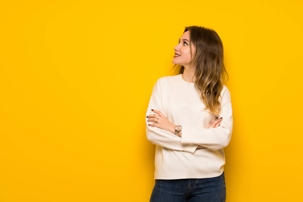 Teenager girl over yellow wall keeping the arms crossed while smiling - Photo, Image