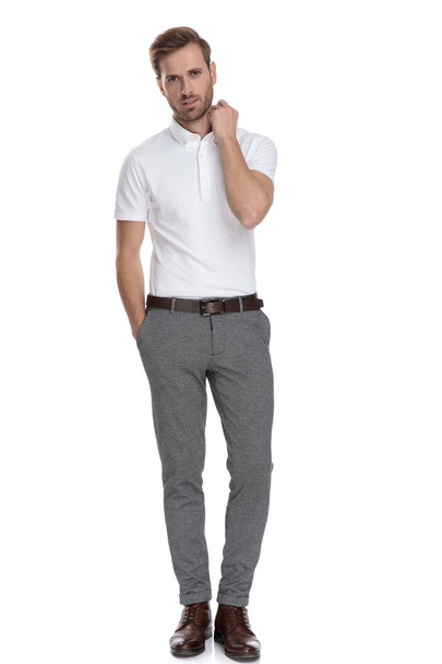 full body picture of a young casual man fixing his collar while standing on white background - Φωτογραφία, εικόνα