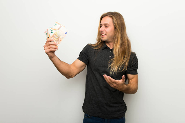 Blond man with long hair over white wall taking a lot of money - Foto, imagen