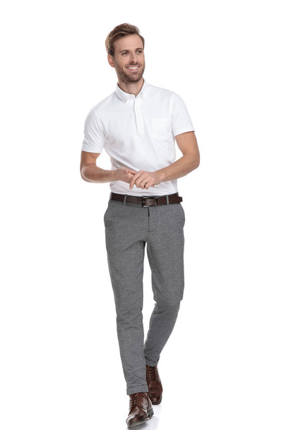 confident young casual man holding palms together is walking and looks to side on white background - Zdjęcie, obraz