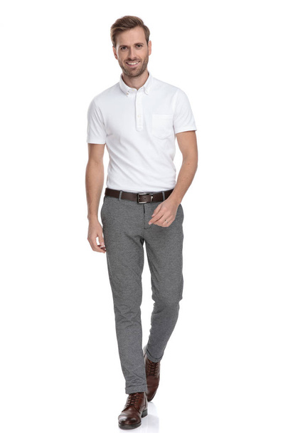 confident young casual man is walking forward on white background - Φωτογραφία, εικόνα