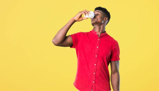 junger afrikanisch-amerikanischer Mann trinkt heißen Kaffee in Pappbecher zum Mitnehmen auf gelbem Hintergrund - Foto, Bild