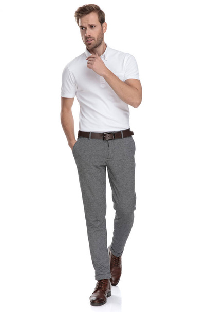 smart casual man with hand in pocket is walking and thinking while looking away to side on white background - Photo, Image