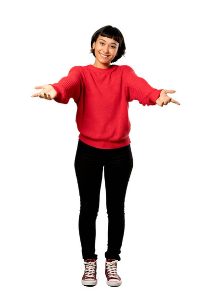A full-length shot of a Short hair girl with red sweater presenting and inviting to come with hand over isolated white background - Photo, image