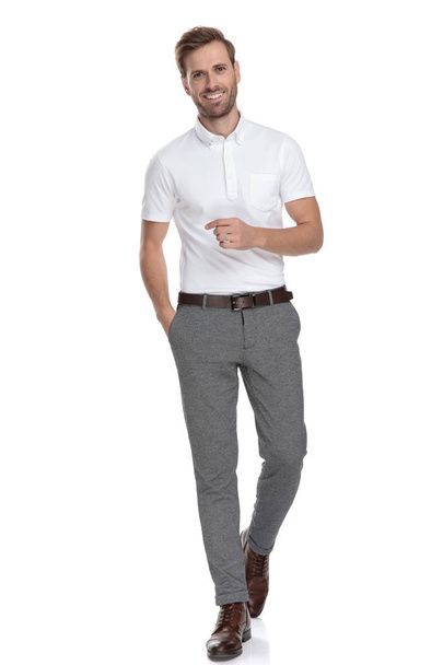 relaxed young casual man is walking forward with hand in pocket on white background - Valokuva, kuva