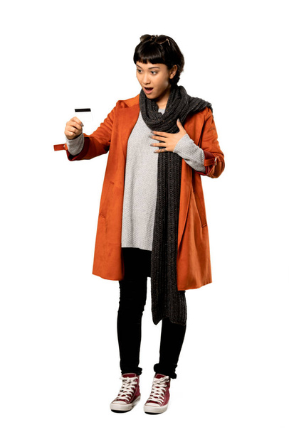 Una foto completa de una mujer de pelo corto con abrigo sosteniendo una tarjeta de crédito y sorprendida sobre un fondo blanco aislado
 - Foto, imagen