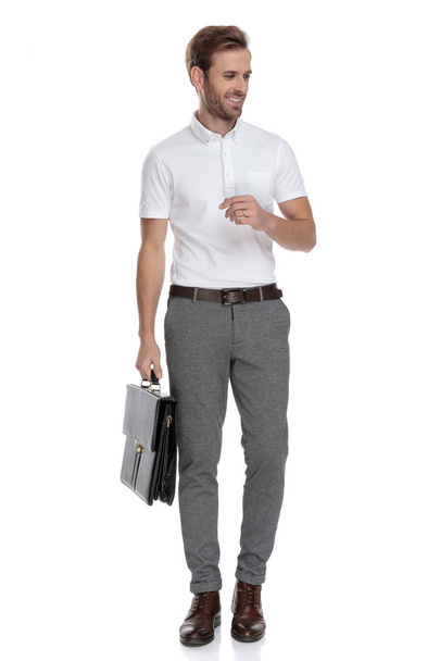 curious smart casual man holding suitcase looks to side on white background - Foto, Bild