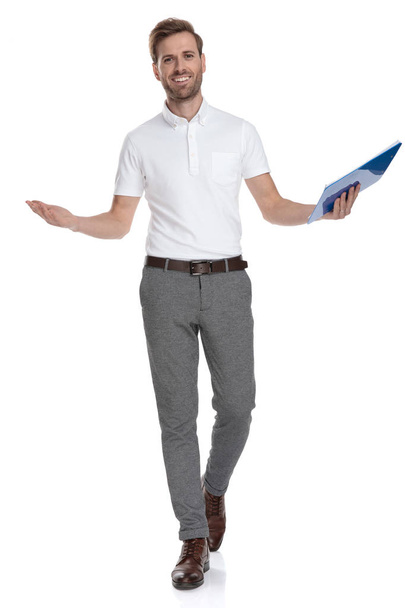 happy casual man holding a clipboard is walking and welcoming on white background - Foto, Imagen
