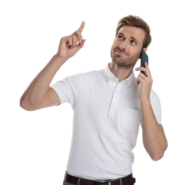 young casual man talking on the phone is pointing up above his head on white background - Foto, Imagem