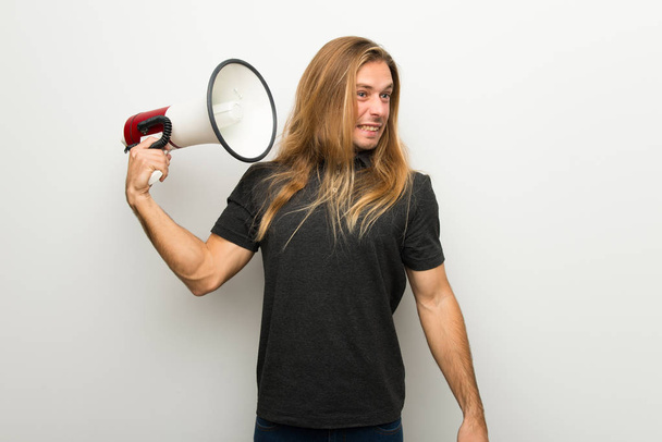 Ξανθός άντρας με μακριά μαλλιά σε λευκό τοίχο, λαμβάνοντας ένα μεγάφωνο που κάνει πολύ θόρυβο - Φωτογραφία, εικόνα