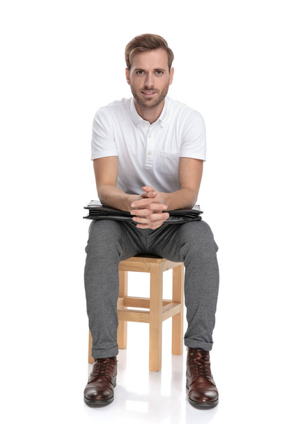 young casual businessman resting on chair with elbows on his briefcase on white background - Photo, Image