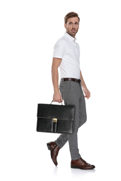 vista laterale di un giovane uomo casuale intrigato che cammina con la sua valigia su sfondo bianco
 - Foto, immagini