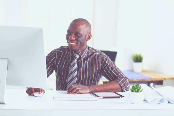 Handsome afro american businessman in classic suit is using a laptop and smiling while working in office - Photo, image