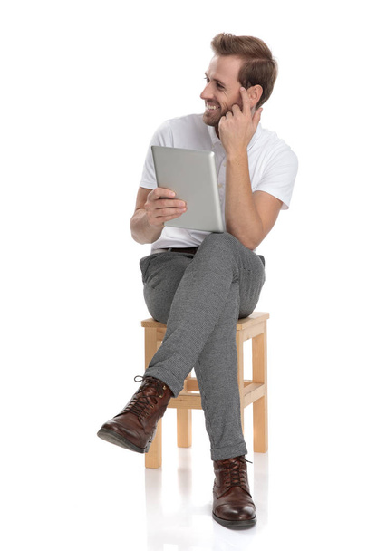 man making the are you crazy gesture to his side while sitting and holding a tablet on white background - Foto, Imagen