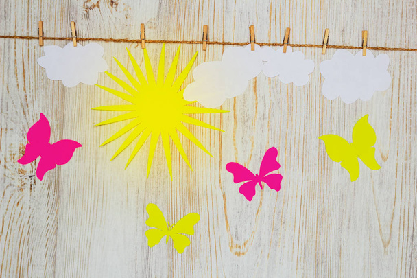 Bel tempo, luminoso concetto giornata di sole. Nuvole, sole e farfalle di carta sono attaccati con mollette. Posa piatta
. - Foto, immagini