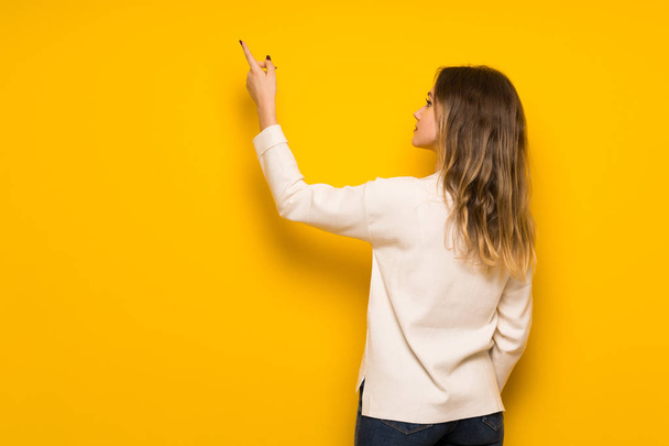 Tiener meisje over gele muur terug met de wijsvinger te wijzen - Foto, afbeelding