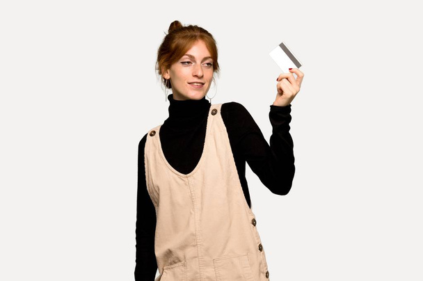 Jeune rousse femme tenant une carte de crédit et réfléchissant sur fond gris
 - Photo, image