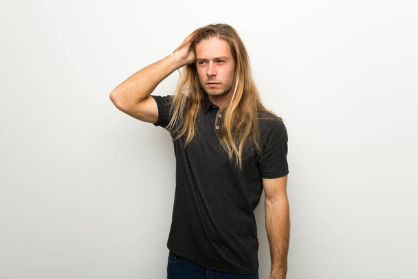 Uomo biondo con i capelli lunghi sul muro bianco sentirsi sconvolto
 - Foto, immagini