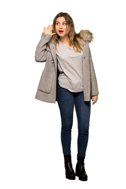 Un plan complet d'une adolescente avec un manteau écoutant quelque chose en mettant la main sur l'oreille sur fond blanc isolé
 - Photo, image