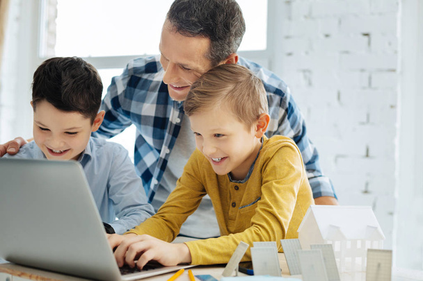 Happy father watching his sons work on laptop - Фото, зображення