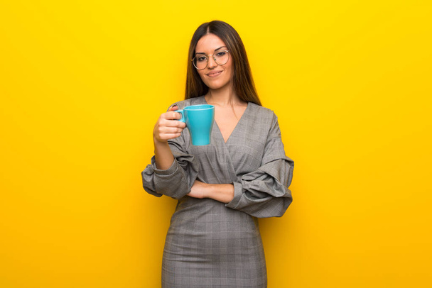 Jovem mulher com óculos sobre a parede amarela segurando uma xícara quente de café
 - Foto, Imagem