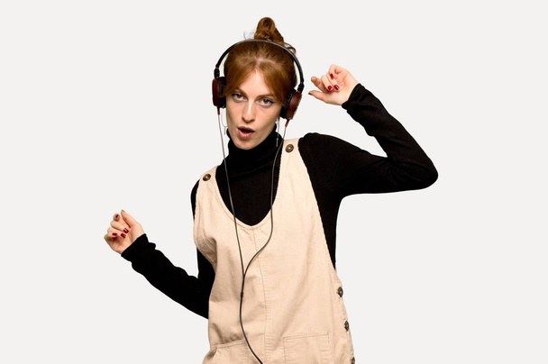 Young redhead woman listening to music with headphones and dancing over grey background - Фото, зображення