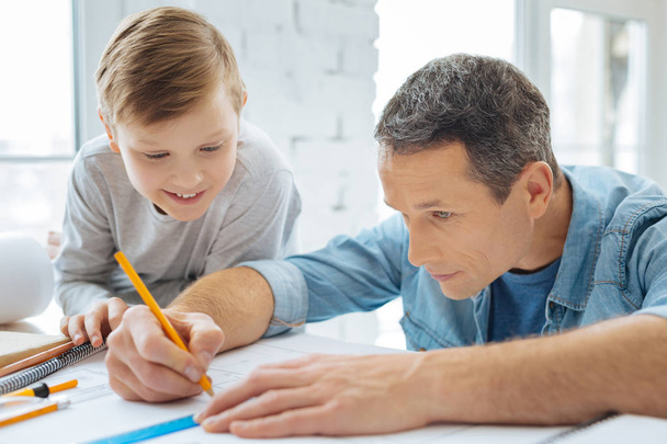 Cheerful boy watching his father sketch blueprint in office - Fotoğraf, Görsel