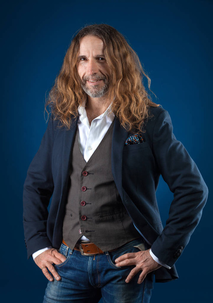 long-haired stylish man in jeans and jacket on a blue background. Studio photography - Photo, Image