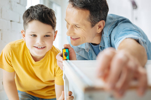 Upbeat father and son measuring width of table - Foto, Bild