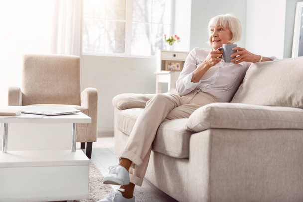 Petite elderly woman drinking coffee in her living room - Fotoğraf, Görsel