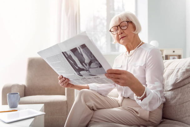 Pretty elderly lady reading a newspaper in living room - Foto, Bild