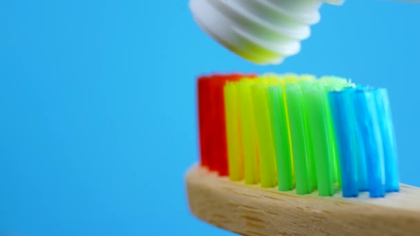 Biała pasta do zębów pochodzących z tubki na rainbow drewniana szczotka - Materiał filmowy, wideo
