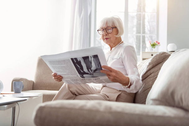 Pretty senior lady being immersed into reading newspaper - Foto, imagen