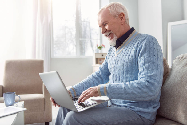 Cheerful elderly man typing on the laptop and smiling - Valokuva, kuva