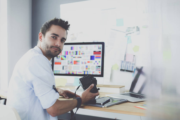 Retrato de jovem designer sentado no estúdio gráfico na frente de laptop e computador enquanto trabalhava online. - Foto, Imagem