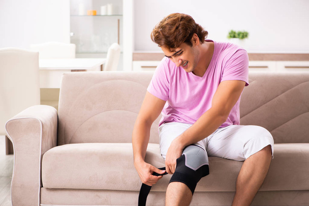 Jonge man met gewonde knie herstellen thuis - Foto, afbeelding
