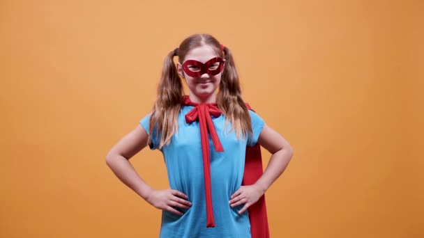 Teini naamioitunut supersankariksi oranssin taustan edessä
 - Materiaali, video
