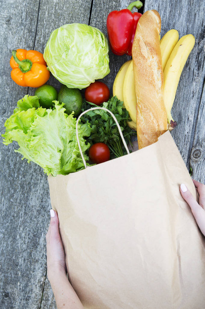 Top view, female hands hold full paper bag of healthy products on rustic wooden table. From above.  - Фото, зображення
