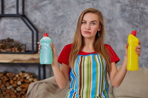 Γυναίκα συγκρίνει δύο μπουκάλι απορρυπαντικού στο σπίτι καθαρισμού στο σαλόνι. Εργασία στο σπίτι. - Φωτογραφία, εικόνα