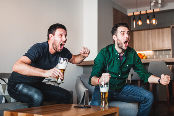 テレビでスポーツを見てビールを飲み 2 人の男します。 - 写真・画像