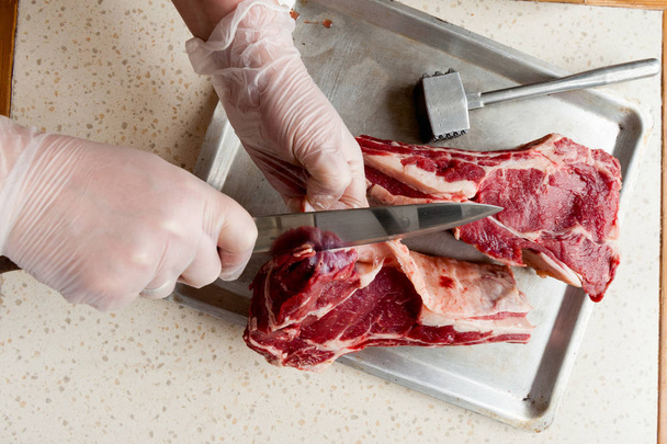 アルミニウム トレイとナイフと手袋をはめた手で霜降り牛肉エッジ - 写真・画像