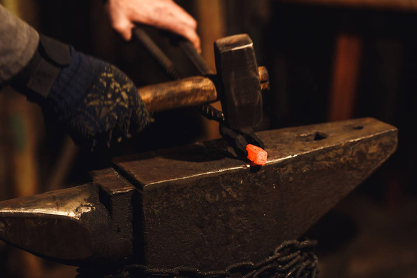 A Kovács, kézzel kovácsolás a vörösen izzó fém az üllőt a kovácsmuhelyben. - Fotó, kép