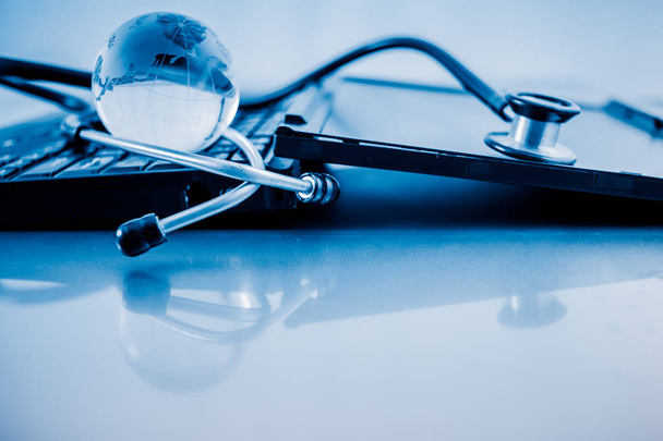 Glass globe and stethoscope on a computer keyboard.blue toned images. - Фото, зображення