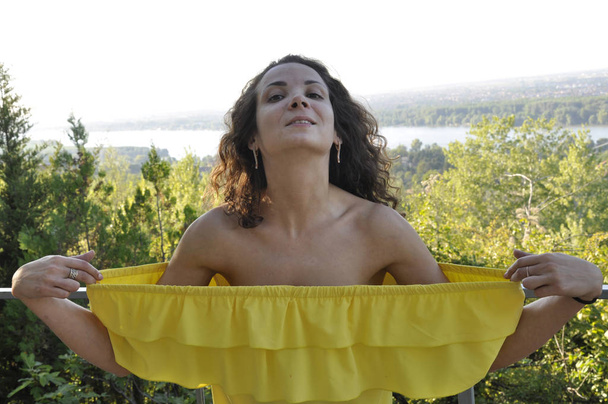 joven feliz rizado de pelo oscuro chica en un vestido amarillo con hombros desnudos
 - Foto, Imagen