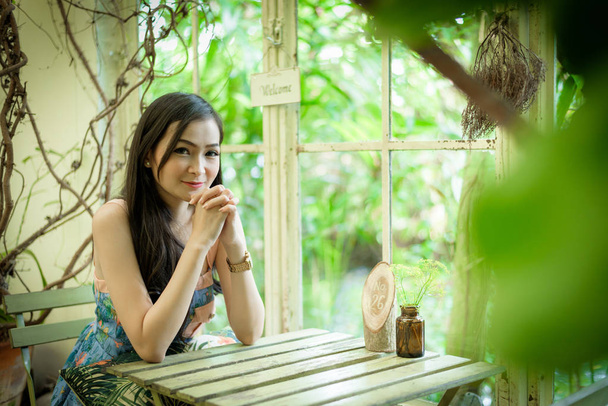 Aziatisch mooi meisje heeft ontspannen met gelukkig en glimlachen in Little Tree Garden cafe, Nakhon Pathom provincie, Thailand in de ochtend. - Foto, afbeelding