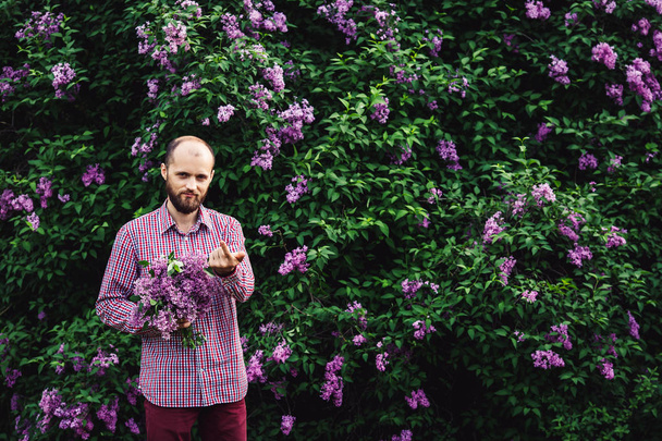 man calls to himself. young bearded man with a bouquet of flowers near lilac blossoms. - Foto, Bild