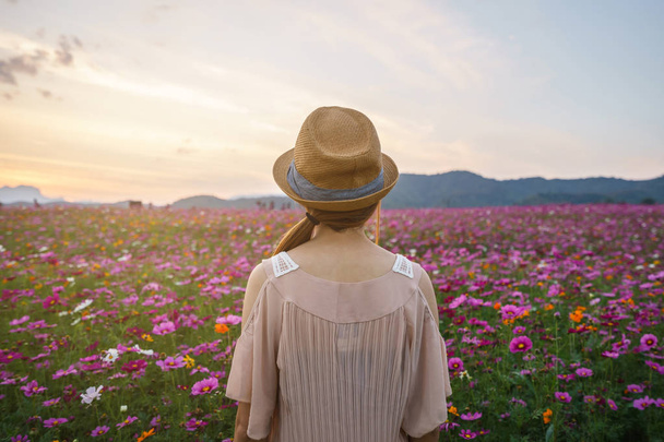 Young woman traveler standing and looking beautiful blooming flowers field - Foto, imagen