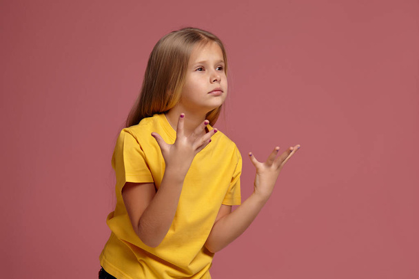 μικρό κορίτσι σε ένα κίτρινο μπλουζάκι. έκπληκτος δείχνει τα χέρια - Φωτογραφία, εικόνα