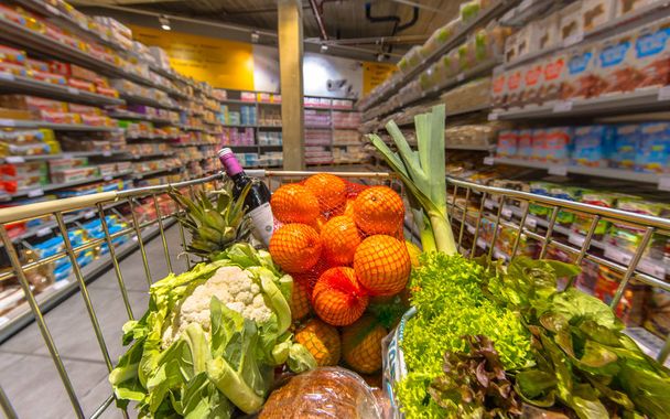 Παντοπωλείων καλάθι τρόλεϊ στο ένα κλίτος σούπερ μάρκετ γεμάτα από προϊόντα υγιεινής διατροφής που προκύπτει από την άποψη τους πελάτες - Φωτογραφία, εικόνα